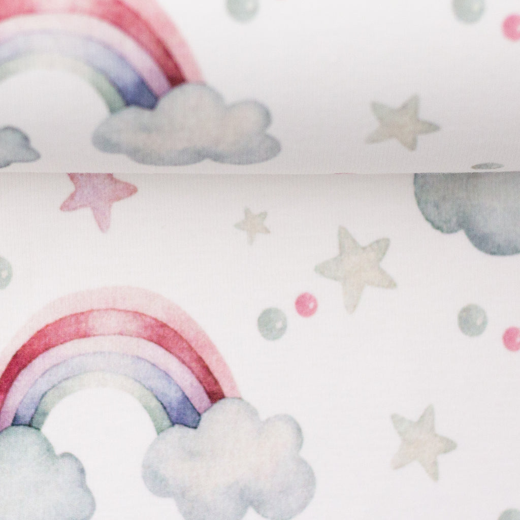 Zu sehen ist eine Nahaufnahme eines weichen, elastischen Baumwolljersey-Stoffs in weiß mit Regenbogen-Motiven, der durch seine angenehme, glatte Oberfläche ideal für Kleidung, Accessoires und kreative DIY-Projekte geeignet ist.