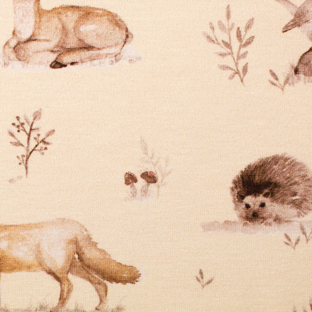 Zu sehen ist eine Nahaufnahme eines weichen, elastischen Baumwolljersey-Stoffs in beige mit Motiven von Waldtieren wie Reh, Fuchs und Hase, der durch seine angenehme, glatte Oberfläche ideal für Kleidung, Accessoires und kreative DIY-Projekte geeignet ist.