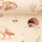 Zu sehen ist eine Nahaufnahme eines weichen, elastischen Baumwolljersey-Stoffs in beige mit Motiven von Waldtieren wie Reh, Fuchs und Hase, der durch seine angenehme, glatte Oberfläche ideal für Kleidung, Accessoires und kreative DIY-Projekte geeignet ist.