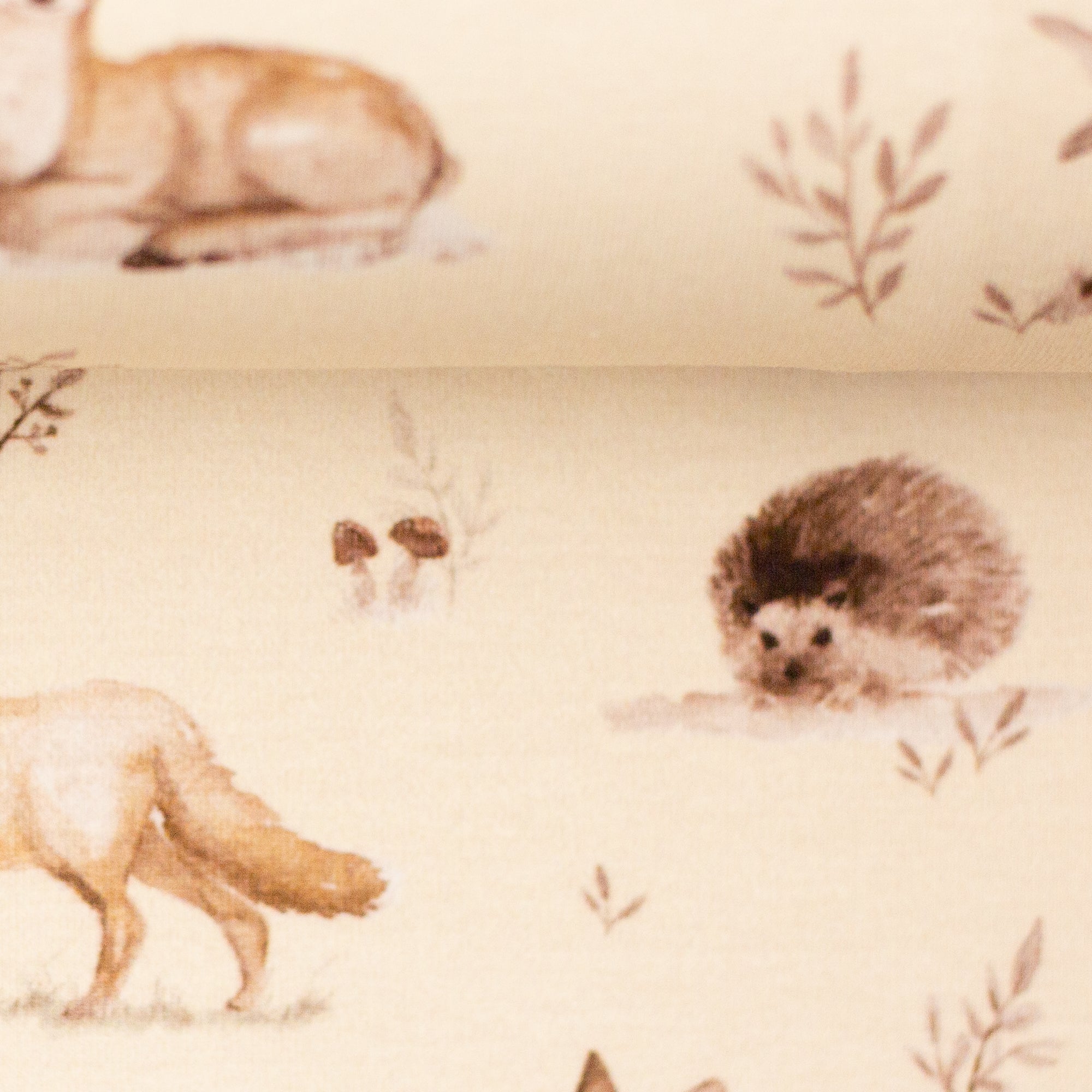 Zu sehen ist eine Nahaufnahme eines weichen, elastischen Baumwolljersey-Stoffs in beige mit Motiven von Waldtieren wie Reh, Fuchs und Hase, der durch seine angenehme, glatte Oberfläche ideal für Kleidung, Accessoires und kreative DIY-Projekte geeignet ist.
