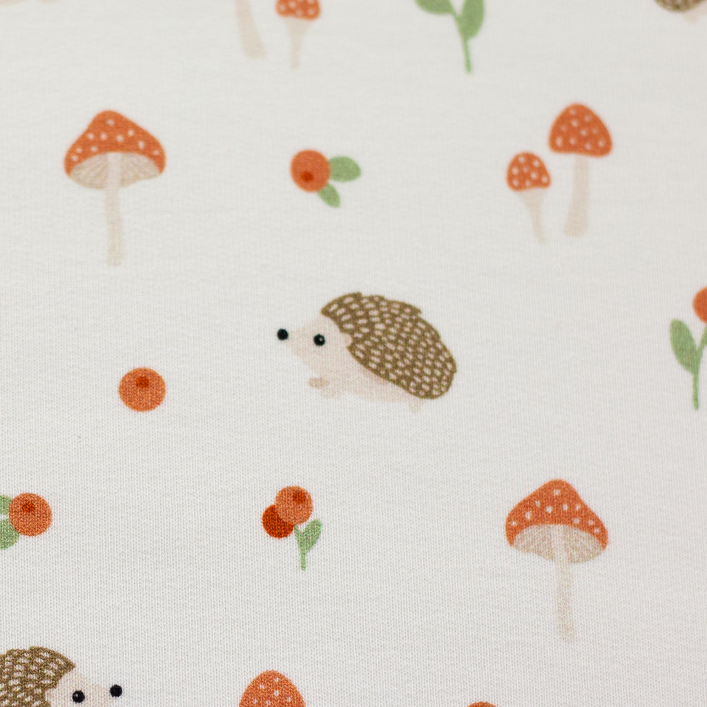 Zu sehen ist eine Nahaufnahme eines weichen, elastischen Baumwolljersey-Stoffs in weiß mit niedlichen Igeln in Naturfarben, der durch seine angenehme, glatte Oberfläche ideal für Kleidung, Accessoires und kreative DIY-Projekte geeignet ist.
