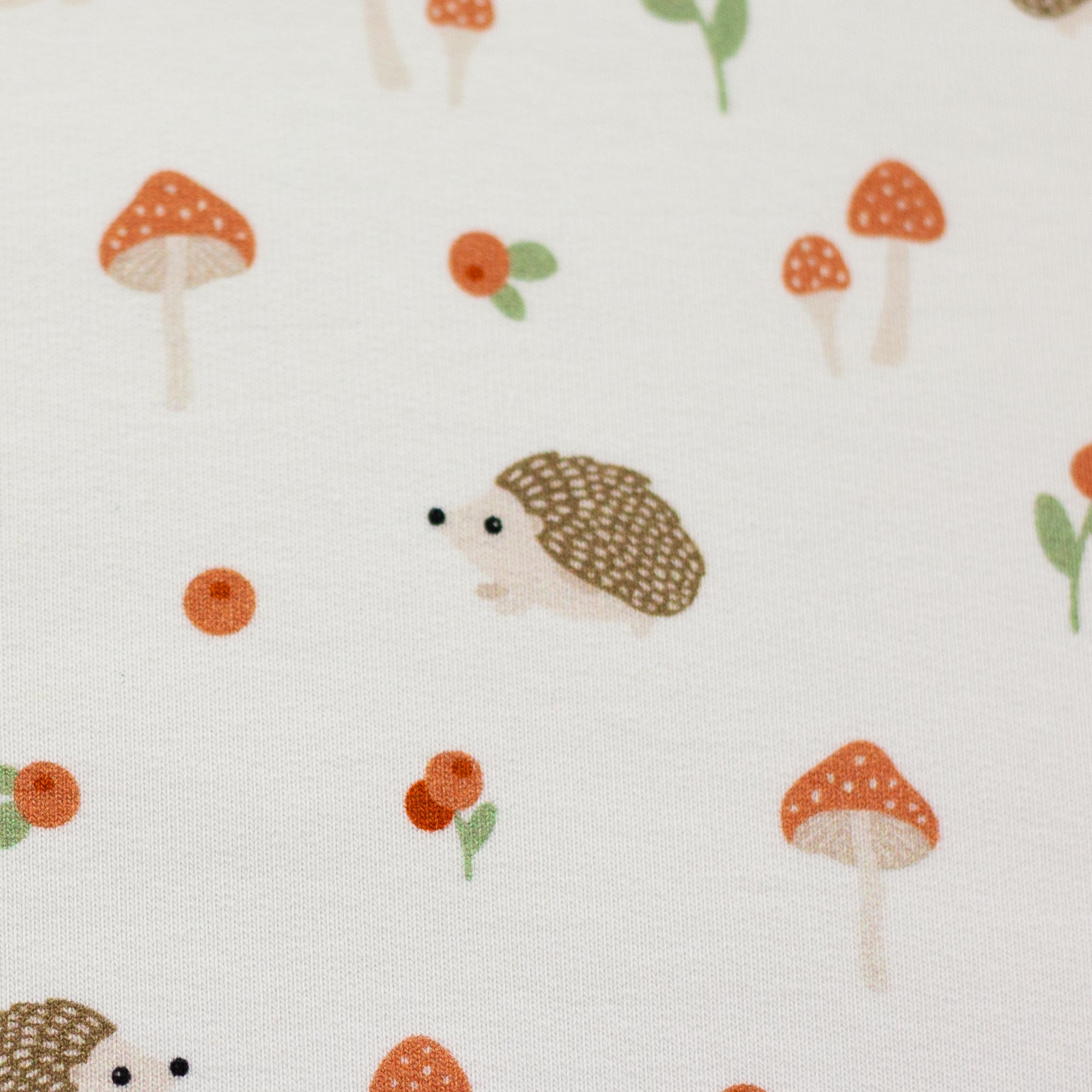 Zu sehen ist eine Nahaufnahme eines weichen, elastischen Baumwolljersey-Stoffs in weiß mit niedlichen Igeln in Naturfarben, der durch seine angenehme, glatte Oberfläche ideal für Kleidung, Accessoires und kreative DIY-Projekte geeignet ist.
