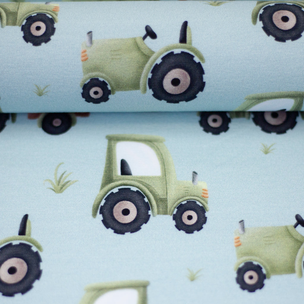 Zu sehen ist eine Nahaufnahme eines weichen, elastischen Baumwolljersey-Stoffs in blau mit einem kindgerechten Muster aus Trucks, LKWs und weiteren Fahrzeugmotiven, der durch seine glatte und dehnbare Oberfläche ideal für Kleidung, Accessoires und kreative DIY-Projekte geeignet ist.