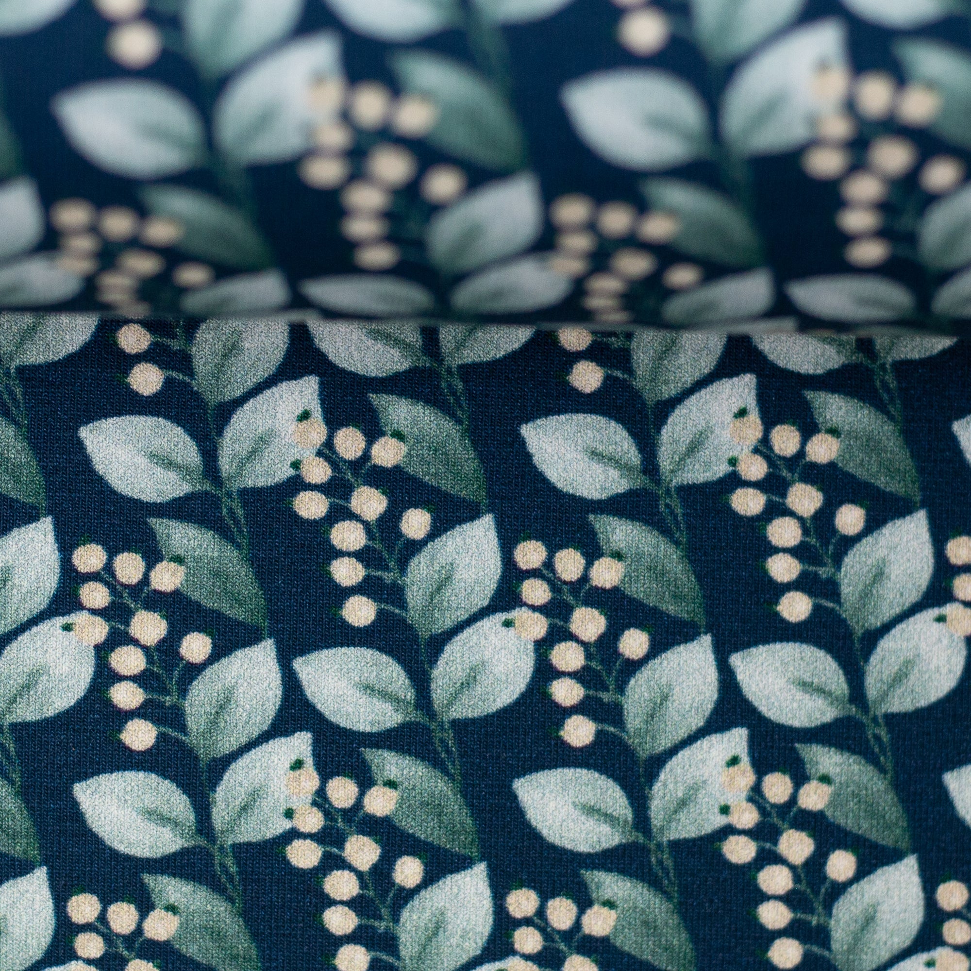 Zu sehen ist eine Nahaufnahme von dunkelblauem Baumwolljersey mit Blättern und Beeren, elastisch und ideal für Kinderkleidung, Accessoires und DIY-Nähprojekte.