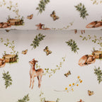 Zu sehen ist eine Nahaufnahme von weißem Baumwolljersey mit Reh- und Waldmotiven, elastisch und ideal für Kinderkleidung und DIY-Nähprojekte.