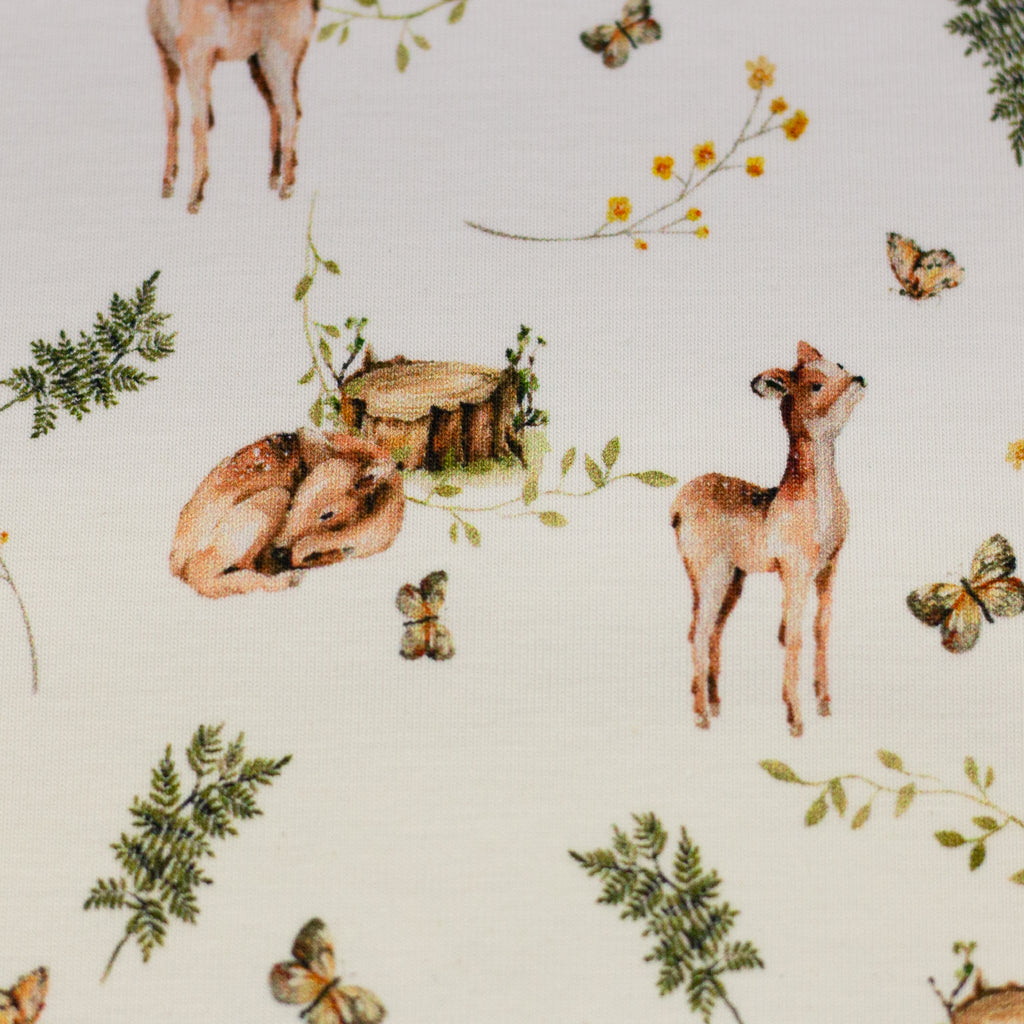 Zu sehen ist eine Nahaufnahme von weißem Baumwolljersey mit Reh- und Waldmotiven, elastisch und ideal für Kinderkleidung und DIY-Nähprojekte.